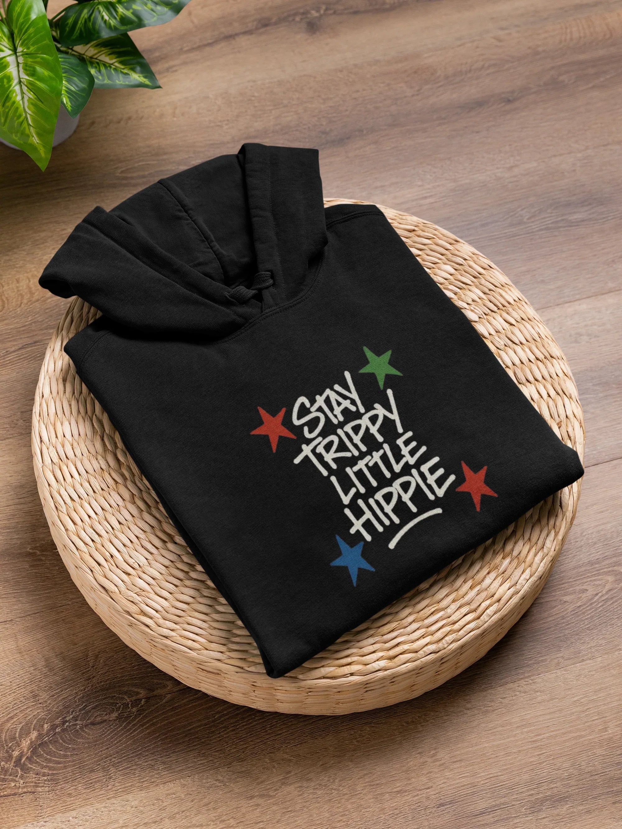 Black hoodie folded on basket with colorful "Stay Trippy Little Hippie" print