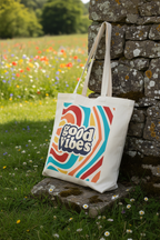 White canvas tote bag with 'good vibes' retro graphic resting against a stone wall
