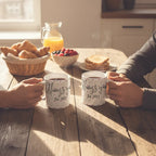 White ceramic mug set, black cursive print and “Est. 2021” on side, held at table.