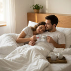 Couple holding white coffee mugs with printed heart and coffee designs on a bed setting