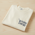 Ivory Birthday Energy T-shirt folded with small chest text graphic and crew neck