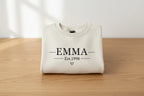 Cream crewneck sweatshirt folded with EMMA Est.1998 text and heart graphic