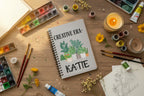 White A5 notebook with spiral binding, plant pots illustration and name KATIE
