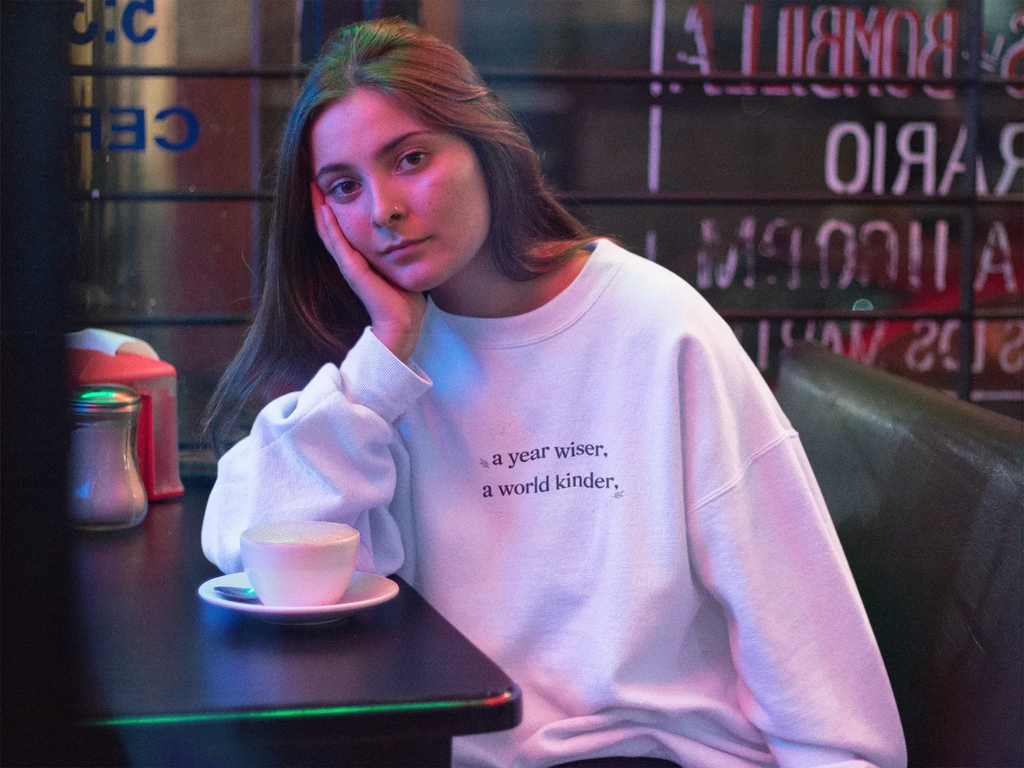 White crewneck sweatshirt with a year wiser, a world kinder print
