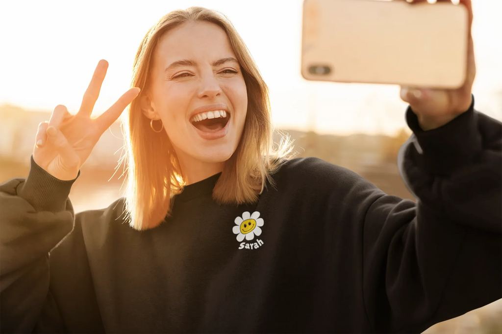 Black crewneck sweatshirt with flower smiley patch, worn by smiling person.