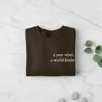Brown sweatshirt with “a year wiser, a world kinder.” front lettering.