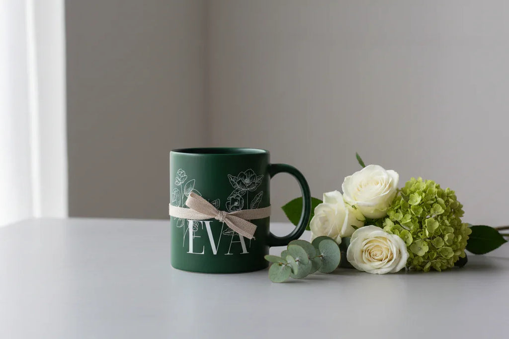 Dark green ceramic mug with floral line art and a personalized name printed on it.