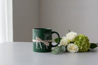 Dark green ceramic mug with floral line art and a personalized name printed on it.