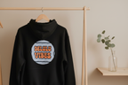 Black pullover hoodie with hood and front pocket, featuring circular retro slogan print