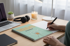 Green spiral notebook on desk with headphones and hand writing with pen