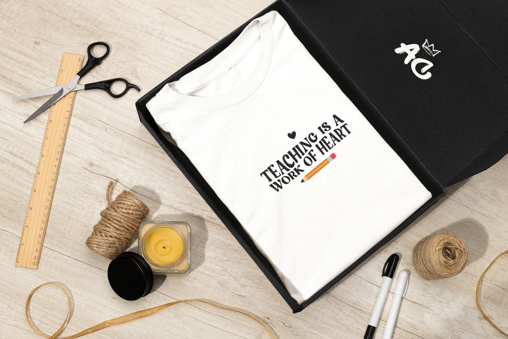 White unisex t-shirt with “Teaching is a work of heart” text and heart icon