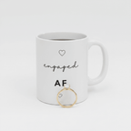 White engagement mug with heart icons and "engaged AF" text; gold ring in front