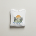 White hoodie folded on flat surface, chest print of mountains and orange sun with blue text