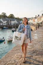 White canvas tote bag held by a person, with personalized script name and watercolor scene