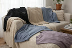 Folded sweatshirt set on sofa: black, sand, and blue crew-necks with small text