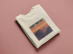 Cream crewneck sweatshirt with “OLDER THAN DIRT.” graphic, folded view