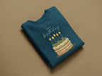 Teal crewneck sweatshirt with “Happy birthday” cake and candle graphic