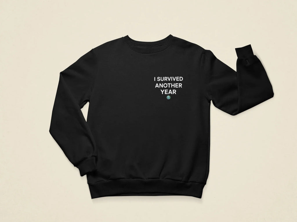 Black crewneck sweatshirt with front text graphic “I SURVIVED ANOTHER YEAR”