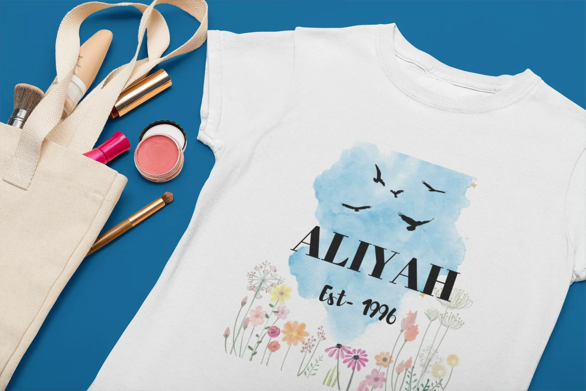 White T-shirt with blue birds, bold name text and floral border.