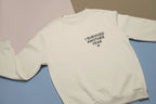 Light cream crewneck sweatshirt with small chest text graphic “I SURVIVED ANOTHER YEAR”