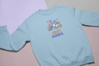 Light blue crewneck sweatshirt with floral crest and 'Sarah's Garden' print.