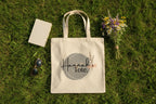 Light canvas tote bag with Hannah's Tote logo and rope handles on grass