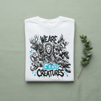 White unisex T-shirt with “We Are God’s Creatures” animal graphic, flat lay.
