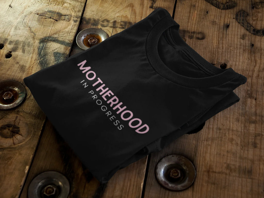 Black heavy cotton maternity T-shirt, folded, with "Motherhood in Progress" print