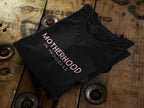 Black heavy cotton maternity T-shirt, folded, with "Motherhood in Progress" print