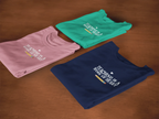 Set of folded unisex T-shirts: mauve, teal, and navy, each with heart slogan print