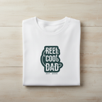 White crewneck graphic T-shirt with green 'REEL COOL DAD' logo, EST 2024