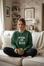 Forest green sweatshirt worn by seated woman, 'TRYING MY BEST' quote on front