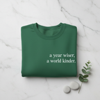 Green sweatshirt with “a year wiser, a world kinder.” text printed on the front.