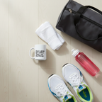 White ceramic coffee mug with black quote, beside a red bottle and towel.