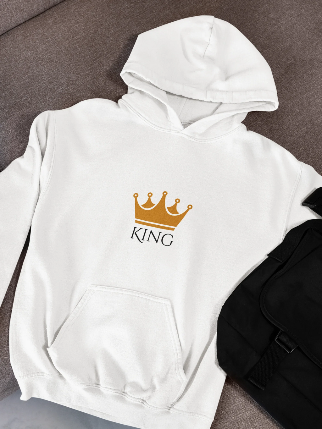 White hooded sweatshirt with KING crown graphic and text on front, folded on couch