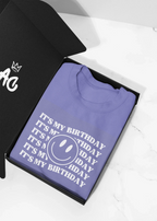 Purple crew hooded sweatshirt folded flat, showing birthday logo graphic print