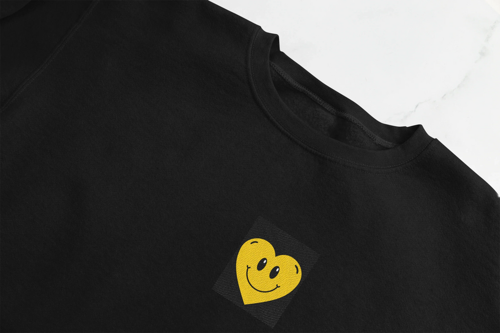 Black crewneck sweatshirt with embroidered smiley heart patch on chest