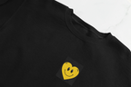 Black crewneck sweatshirt with embroidered smiley heart patch on chest