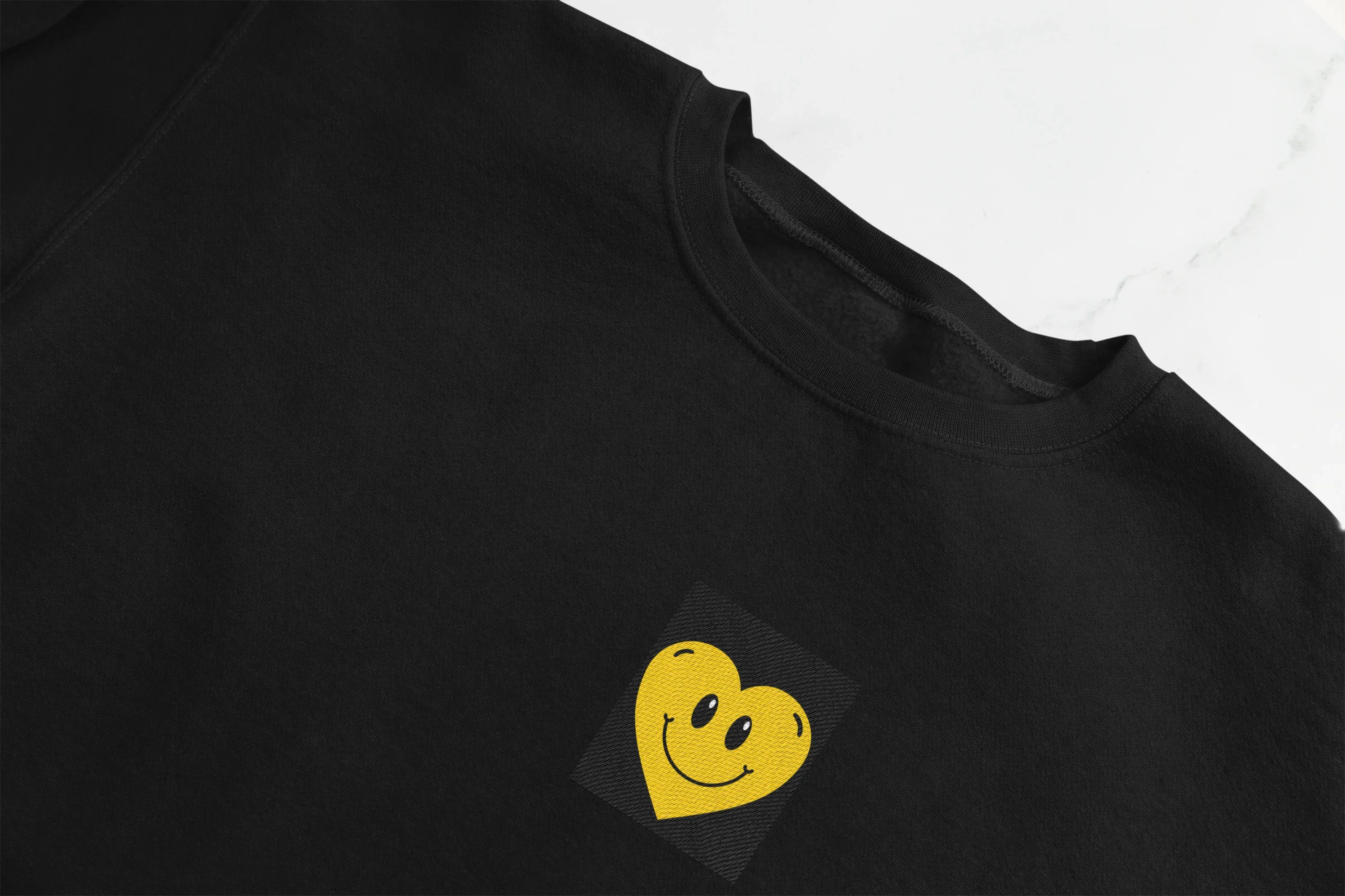 Black crewneck sweatshirt with embroidered smiley heart patch on chest