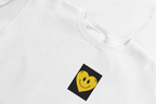 White crewneck sweatshirt with embroidered yellow smiley heart patch on chest