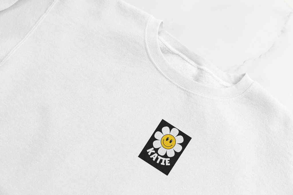White crewneck sweatshirt with small square flower smiley patch at chest.