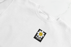 White crewneck sweatshirt with small square flower smiley patch at chest.
