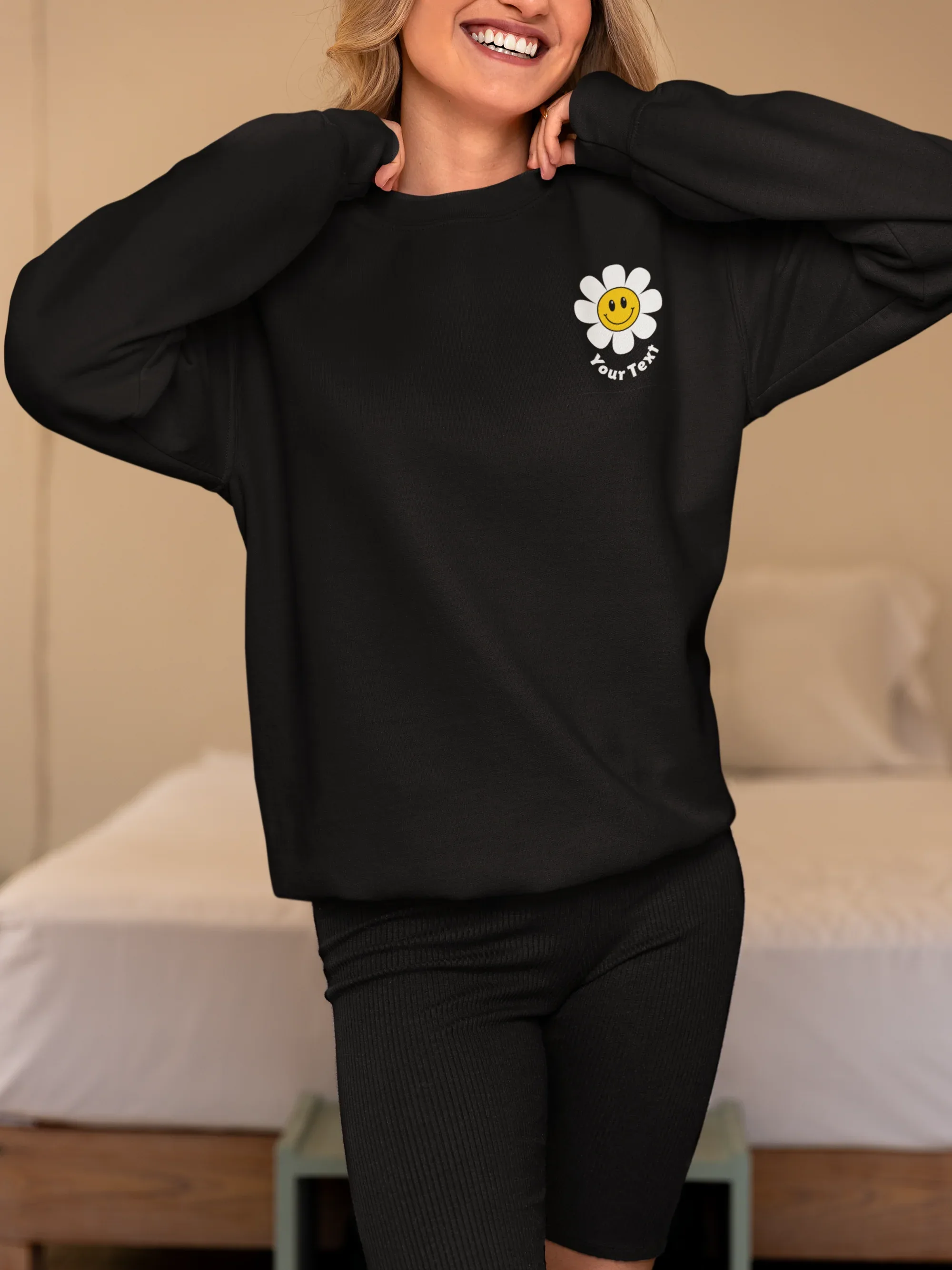 Black crewneck sweatshirt with flower smiley patch on left chest, hands behind neck.