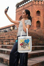 Light canvas tote bag with blue-bordered front print and black handles on outdoor steps
