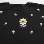 Black sweatshirt with scattered embroidered daisies and center patch reading GRACE