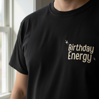 Black crewneck T-shirt with "Birthday Energy" text graphic on the chest