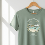 Heather green T-shirt hanging, “OUR HAPPY PLACE” wreath graphic with sea scene and “since 2015”