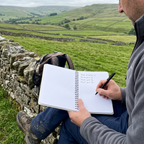 Open A5 nature notebook with white lined pages and black pen, spiral binding