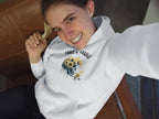 White hooded sweatshirt with front graphic skull and flower design, long sleeves and front pouch pocket.