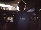 Person wearing a dark navy pullover hoodie with front pocket, hood drawstrings, and logo.